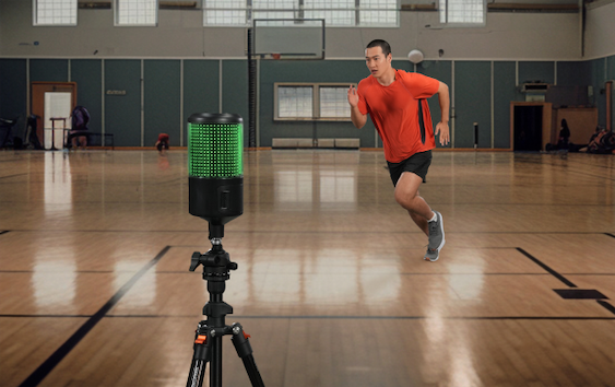 Athlete in red shirt sprinting indoors, monitored by high-tech sports radar device on tripod.